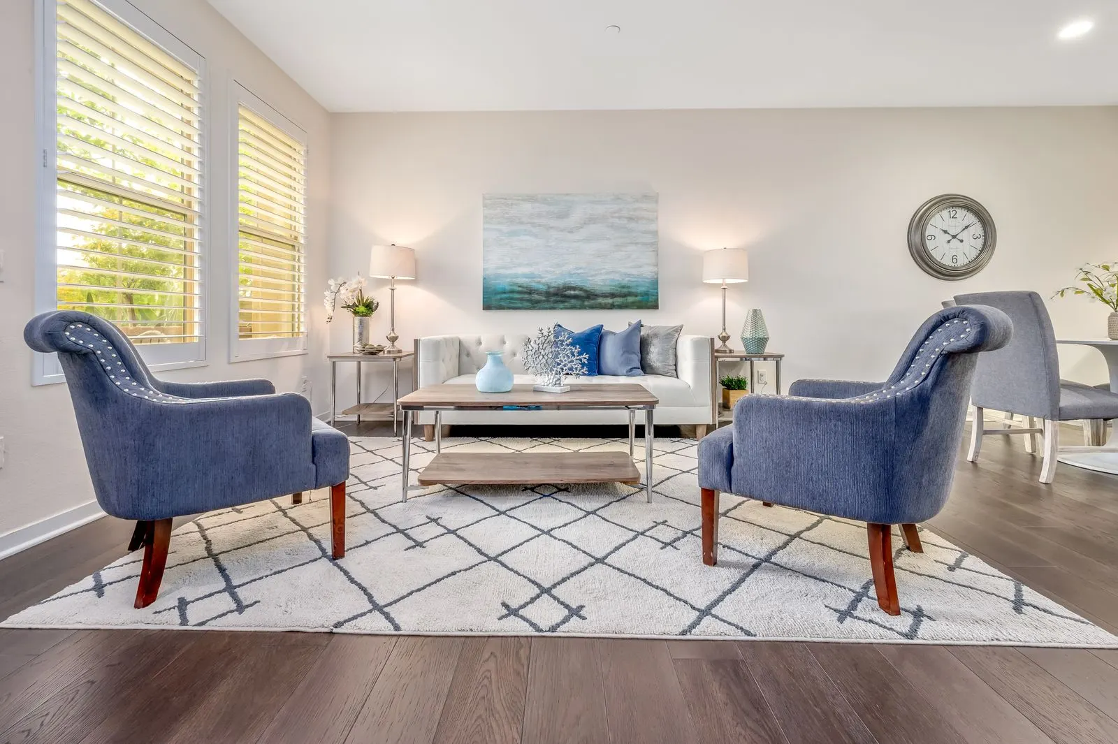 Staged living room with two blue armchairs, a white sofa and bright windows