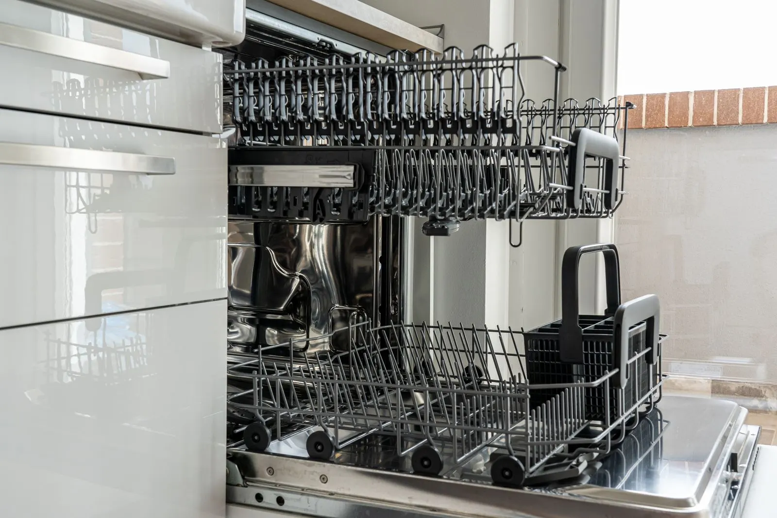 Open dishwasher with empty racks in a sunlit kitchen