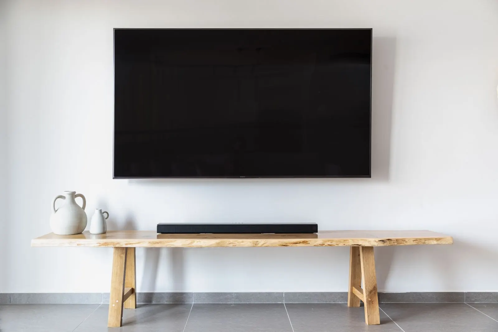 Flat screen TV mounted flush on a white wall above a wooden console